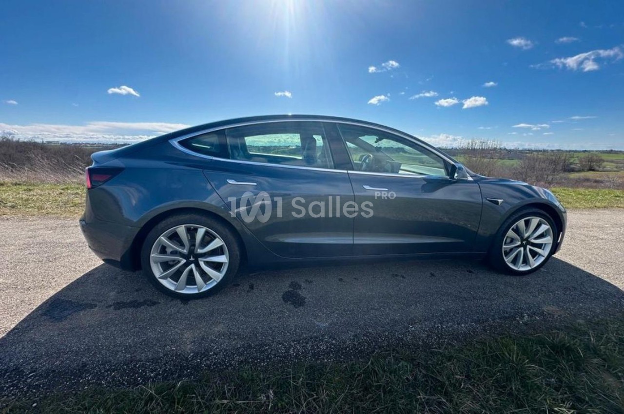 Voiture électrique grise stationnée sur une route de campagne sous un ciel ensoleillé.