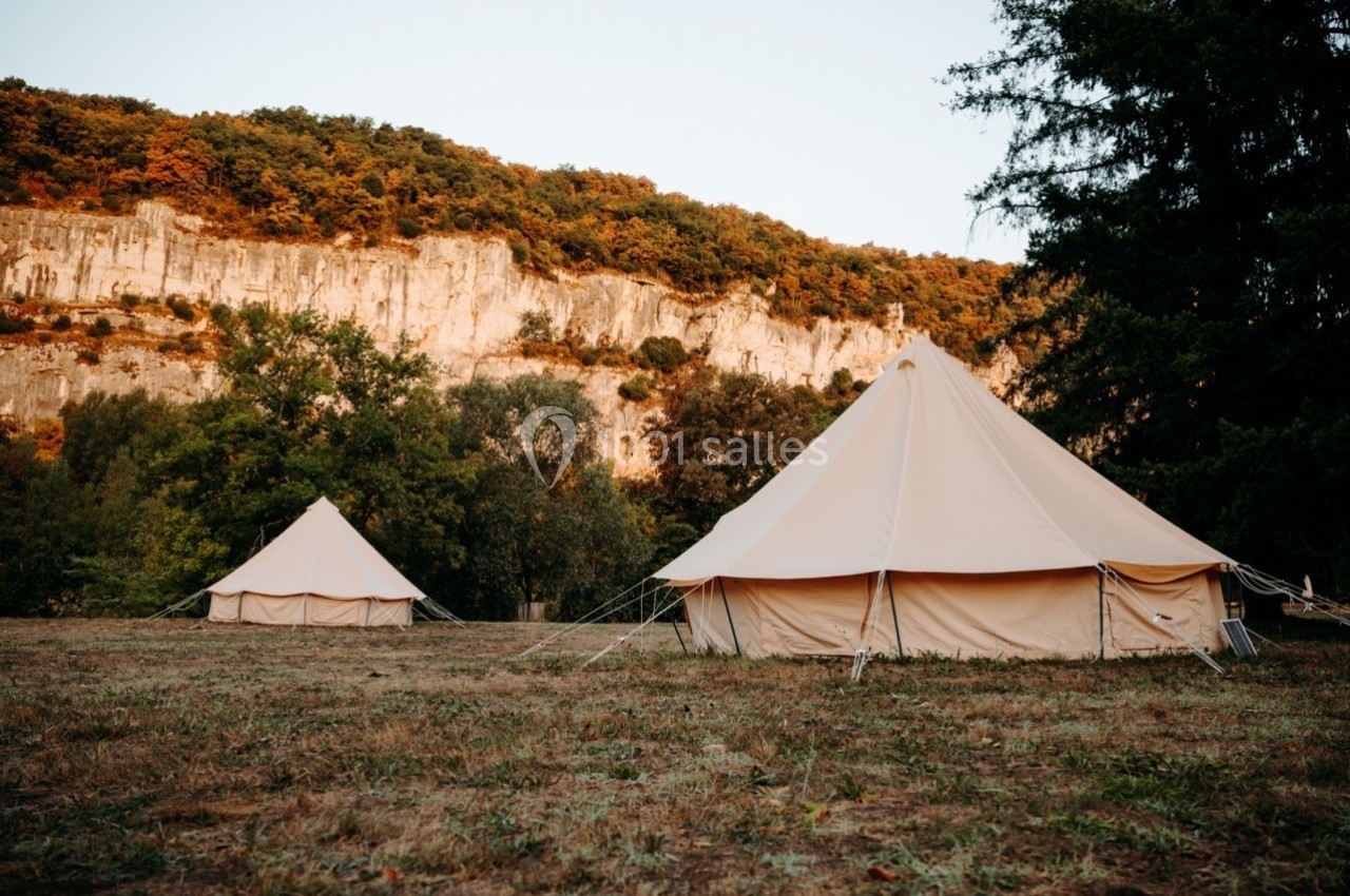 Deux tentes en toile beige installées sur un terrain herbeux, avec une falaise et des arbres en arrière-plan.