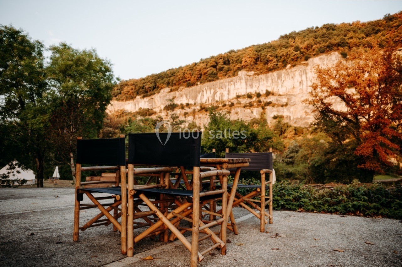 Chaises en bambou autour d'une table sur une terrasse, avec une falaise et des arbres en arrière-plan.