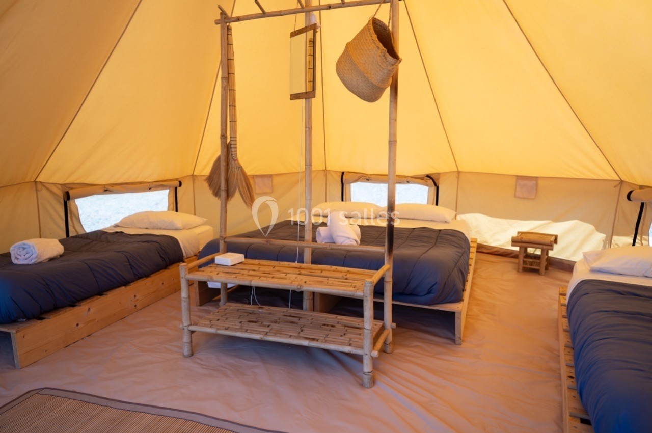 Intérieur d'une tente aménagée avec quatre lits simples, linge de lit bleu et mobilier en bois et bambou.