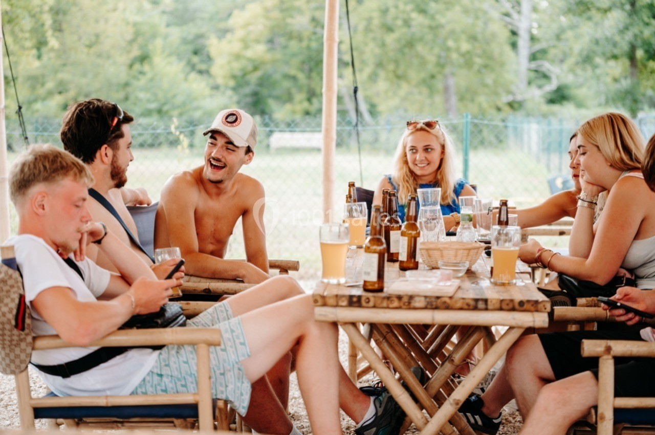 Groupe de jeunes assis autour d'une table en plein air, discutant et partageant des boissons.