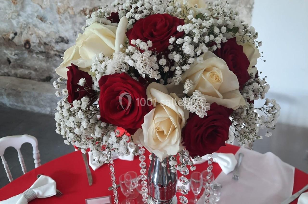 Centre de table avec un bouquet de roses rouges et blanches, gypsophile et perles, sur une nappe rouge.