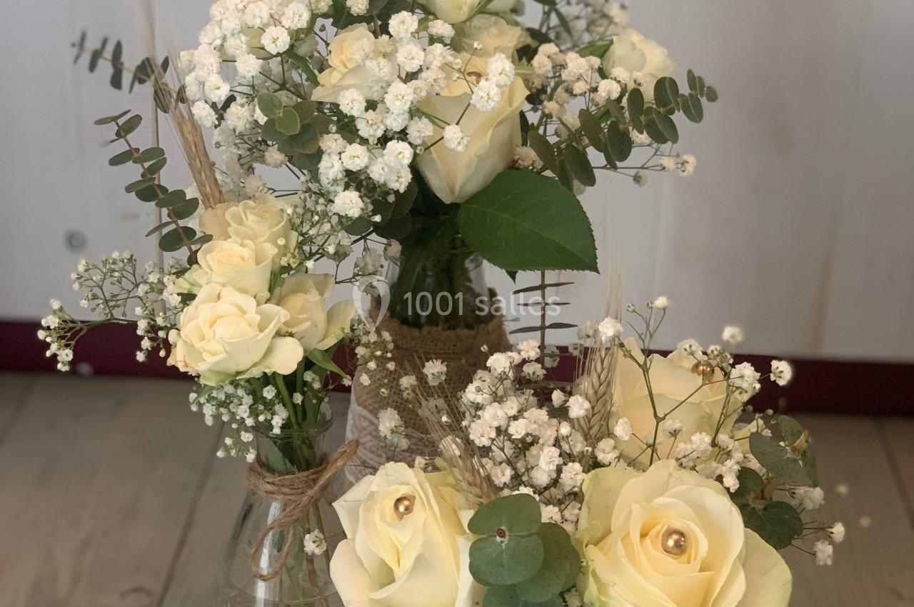Bouquets de roses blanches et gypsophiles dans des vases en verre décorés, posés sur un plateau en bois.
