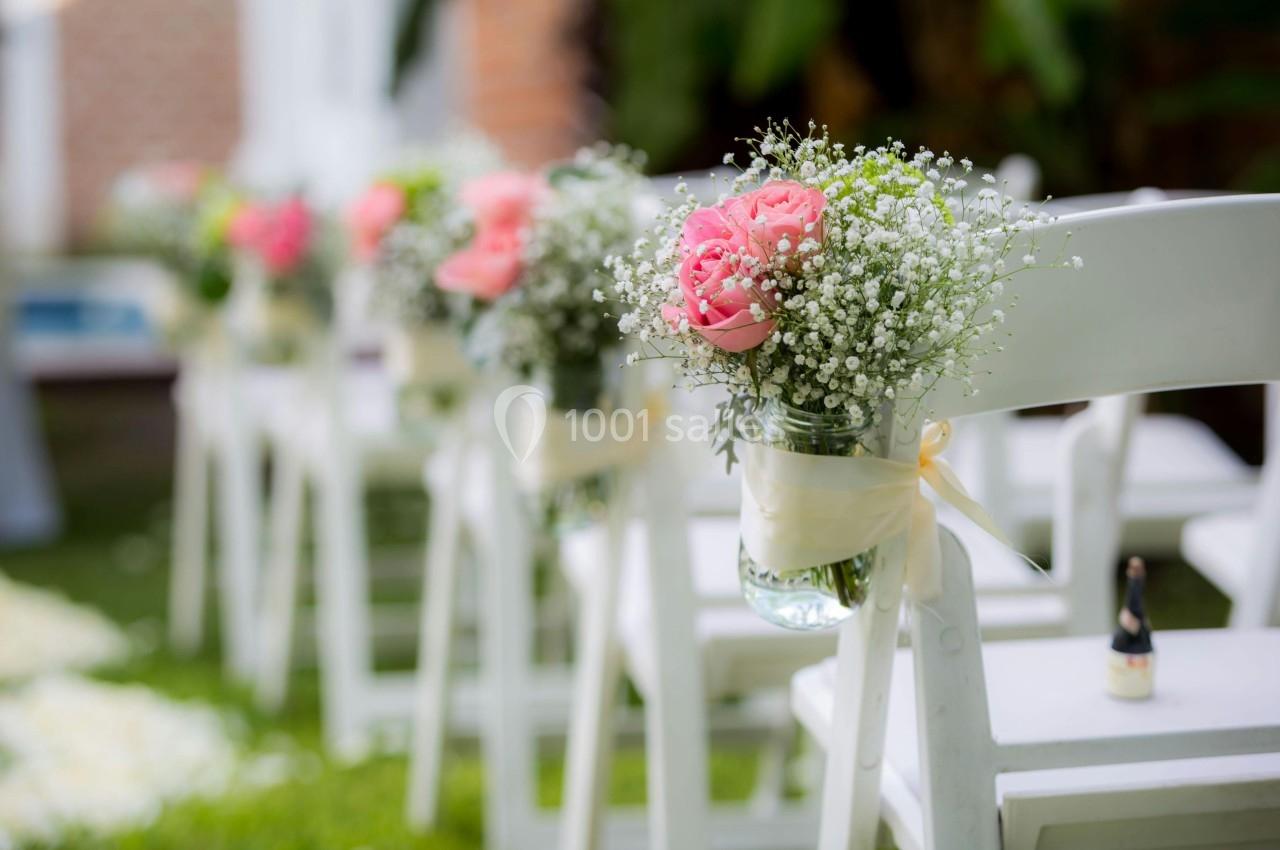 Chaises blanches alignées avec des bouquets de fleurs roses et gypsophiles attachés, disposées sur une pelouse.