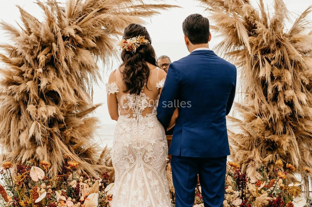 Un couple de dos échange ses vœux devant un décor floral avec des pampas et des fleurs séchées.