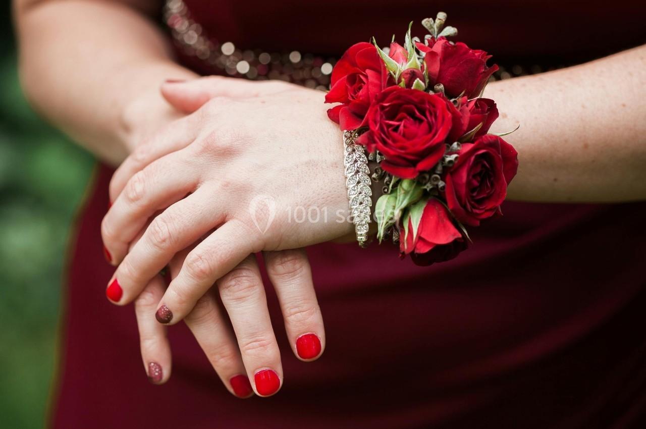 Mains croisées d'une femme portant un bracelet scintillant et un corsage de roses rouges sur une robe assortie.