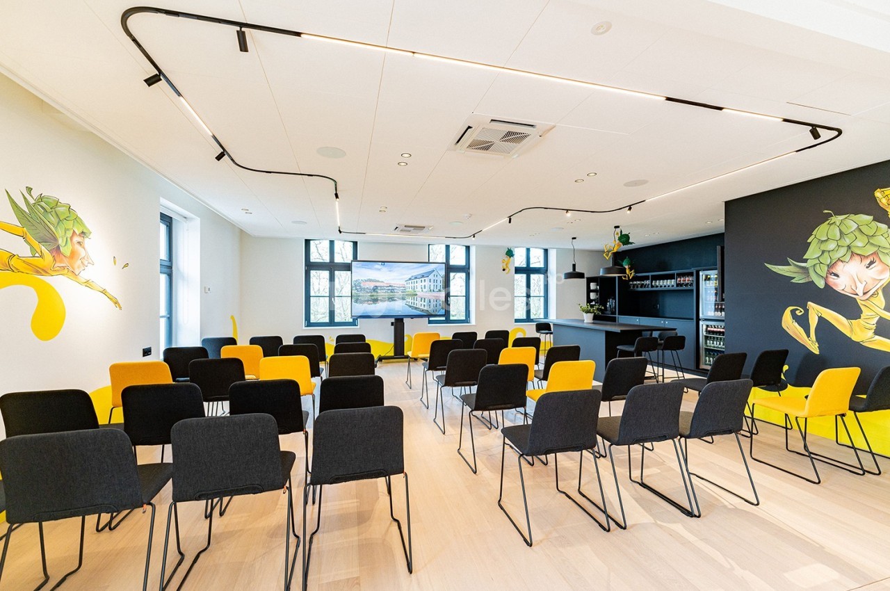 Salle de conférence lumineuse avec des chaises noires et jaunes, un bar au fond et des illustrations murales colorées.