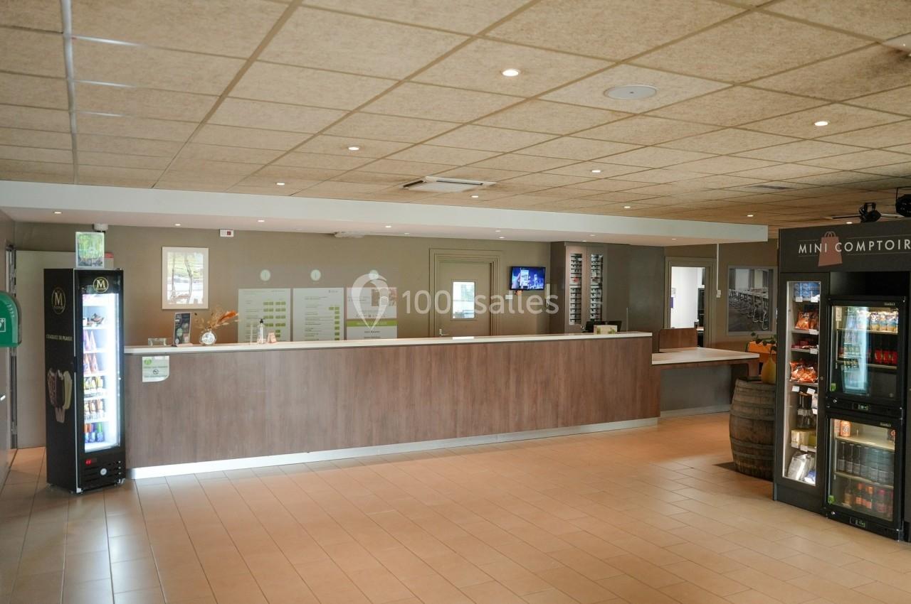 Accueil d'un établissement avec un comptoir en bois, des distributeurs automatiques et un sol en carrelage beige.