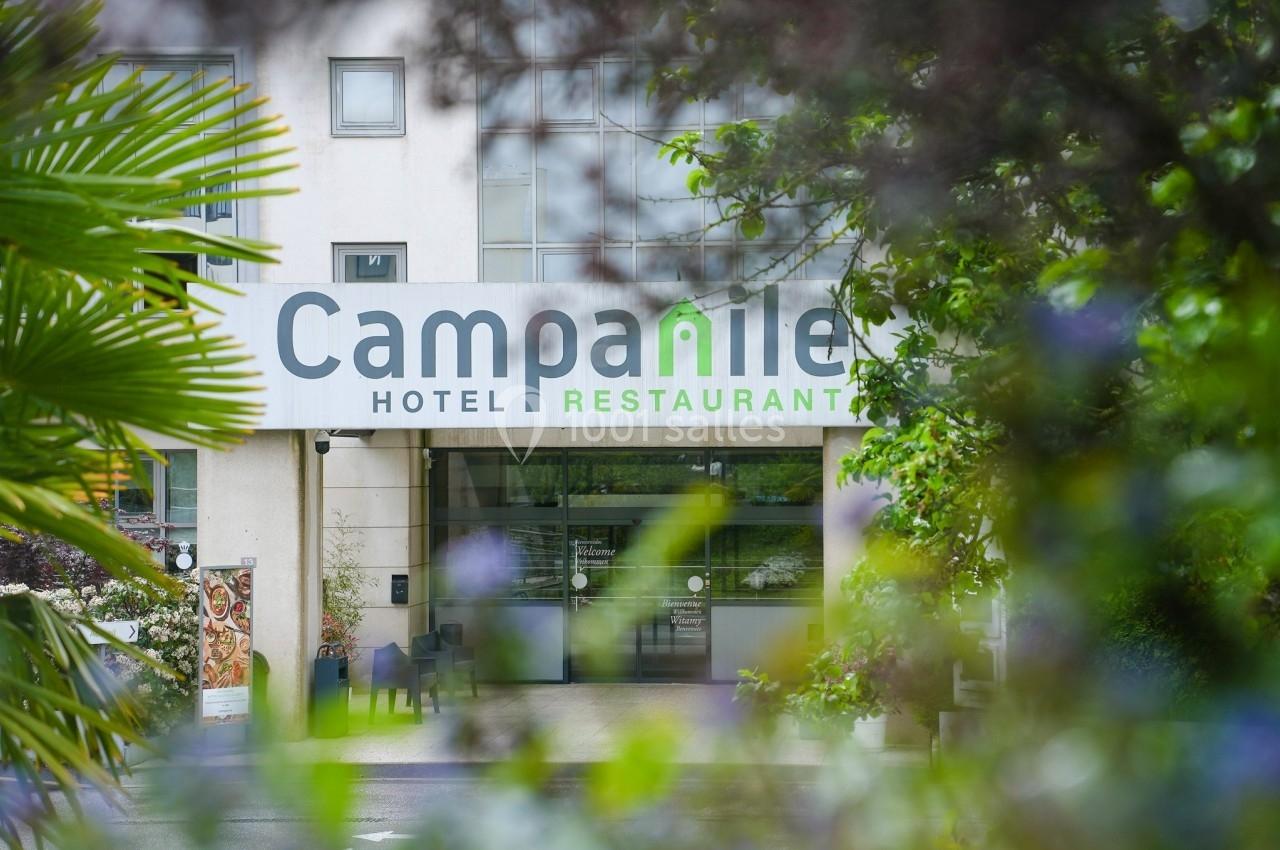 Façade d'un hôtel-restaurant Campanile entourée de végétation, avec une entrée vitrée visible.