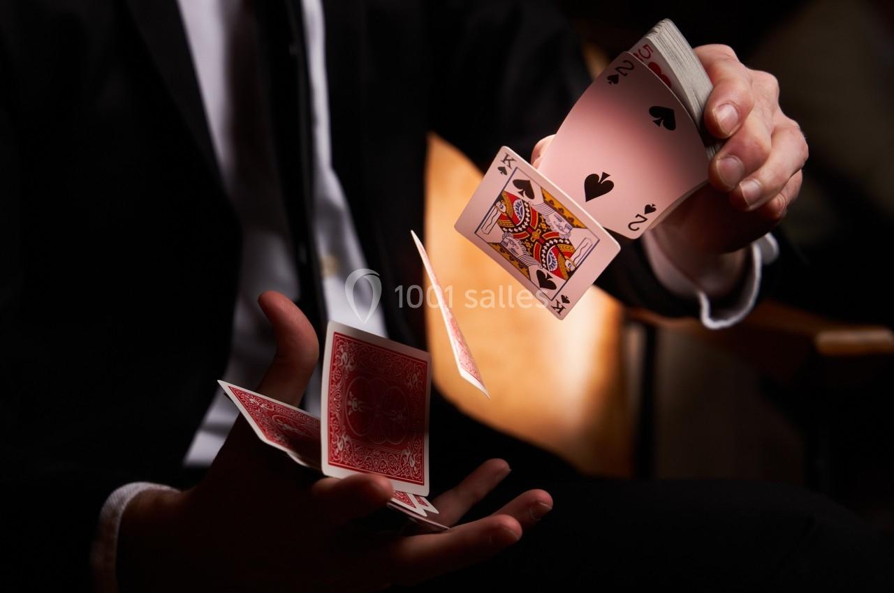 Un magicien en costume manipule des cartes à jouer en plein mouvement dans un environnement sombre.