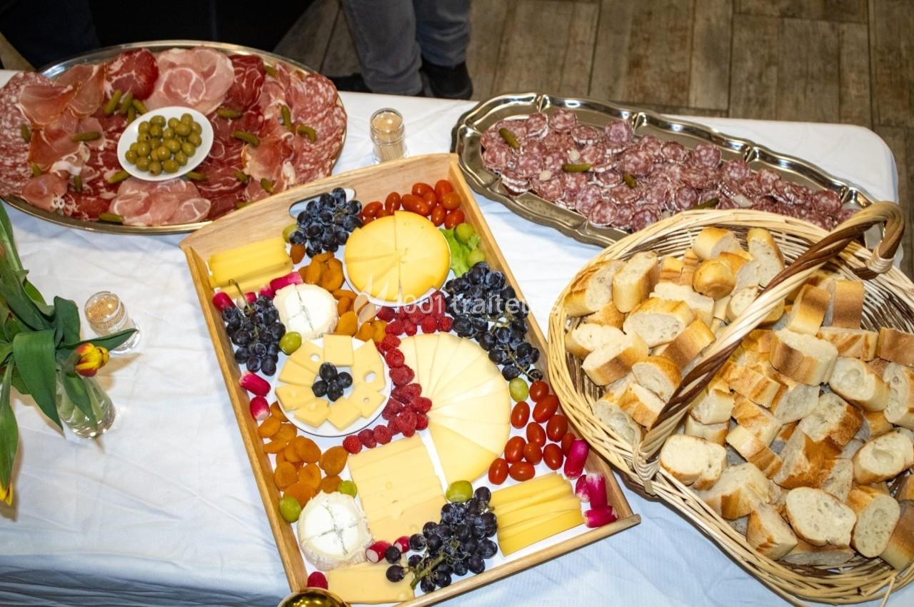 Plateau de fromages, fruits et charcuteries disposés sur une table avec un panier de pain et des plats garnis.