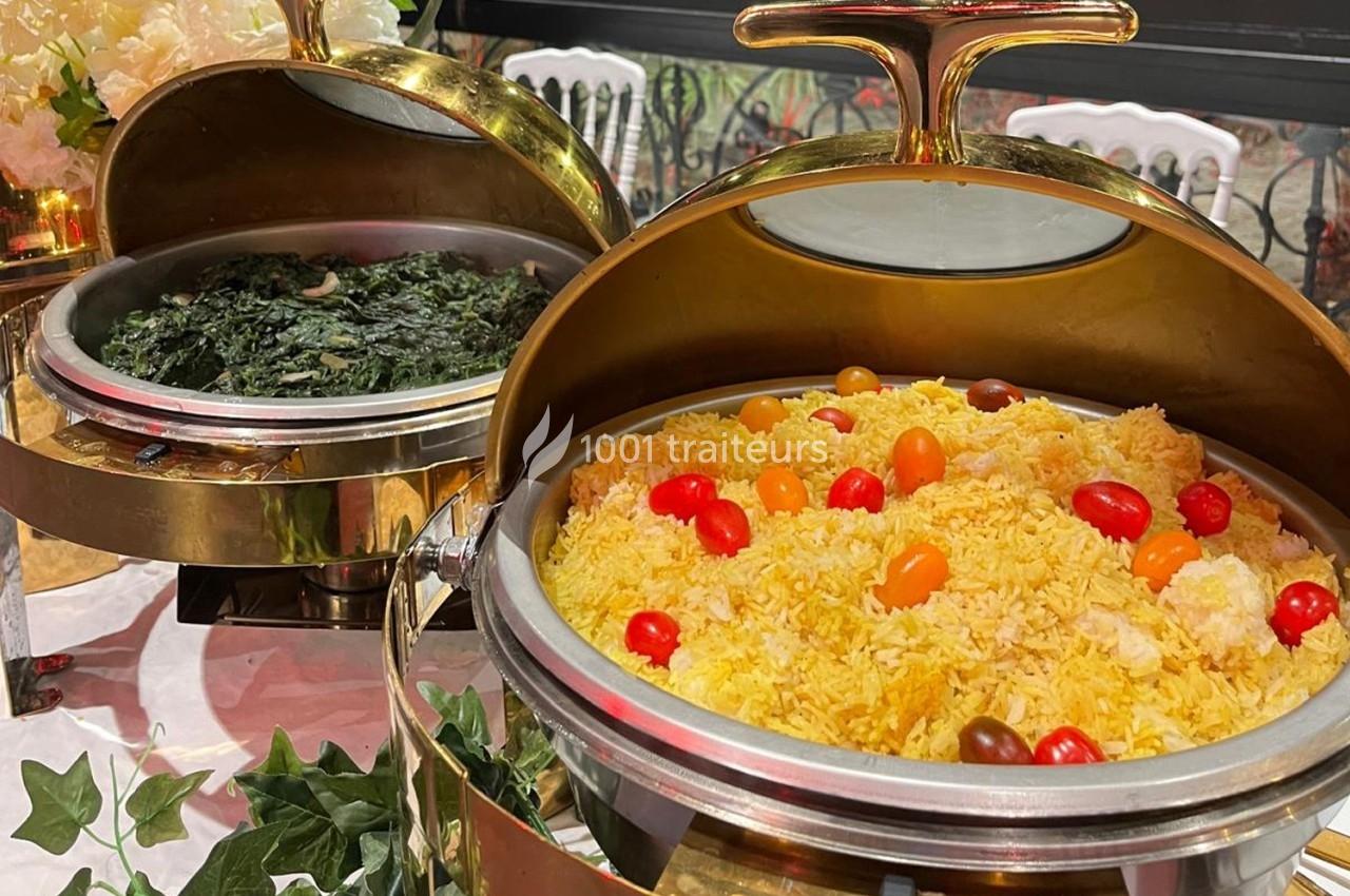 Buffet avec un plat de riz jaune garni de tomates cerises et un plat d'épinards dans des récipients en métal doré.