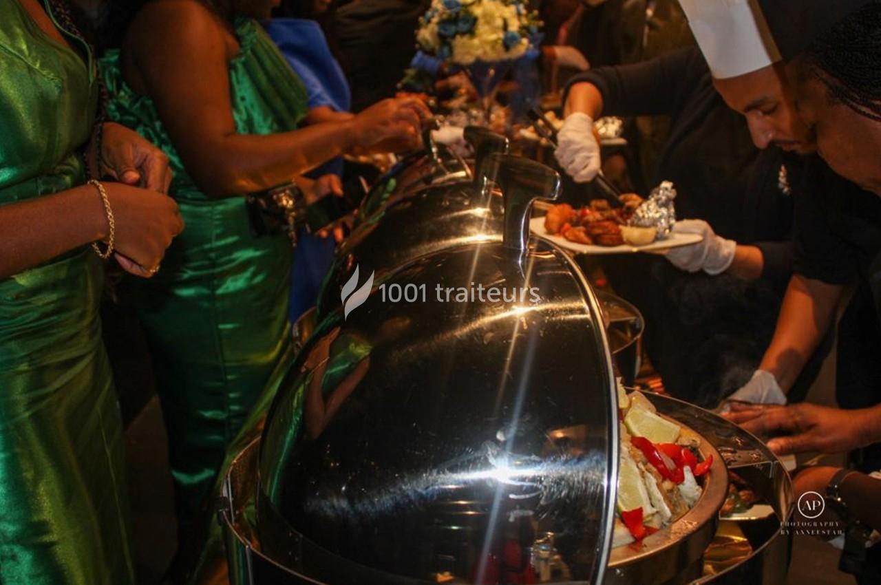 Des convives se servent à un buffet avec des plats chauds sous des cloches en métal, encadrés par un chef.