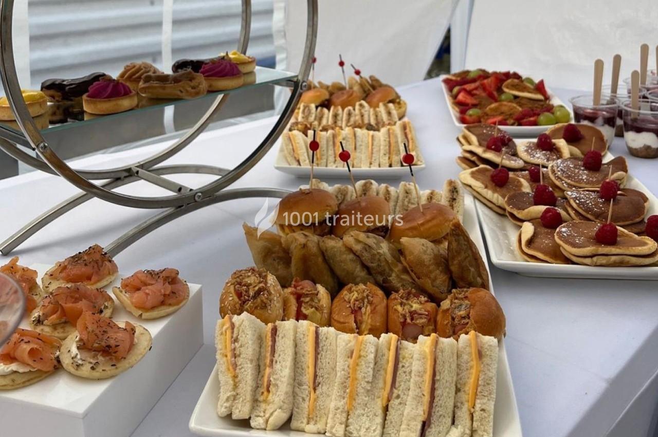 Buffet composé de sandwichs, viennoiseries, fruits, pancakes et verrines, présenté sur une table blanche.