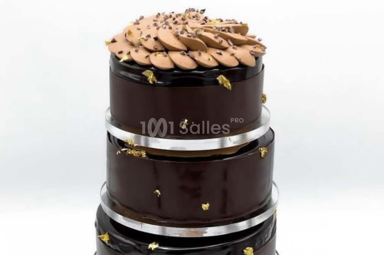Gâteau à trois étages recouvert de glaçage au chocolat brillant, décoré de touches dorées et d'une garniture chocolatée.