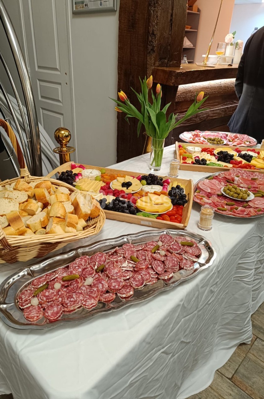 Table dressée avec des plateaux de charcuterie, fromages, fruits, pain et un bouquet de tulipes en décoration.