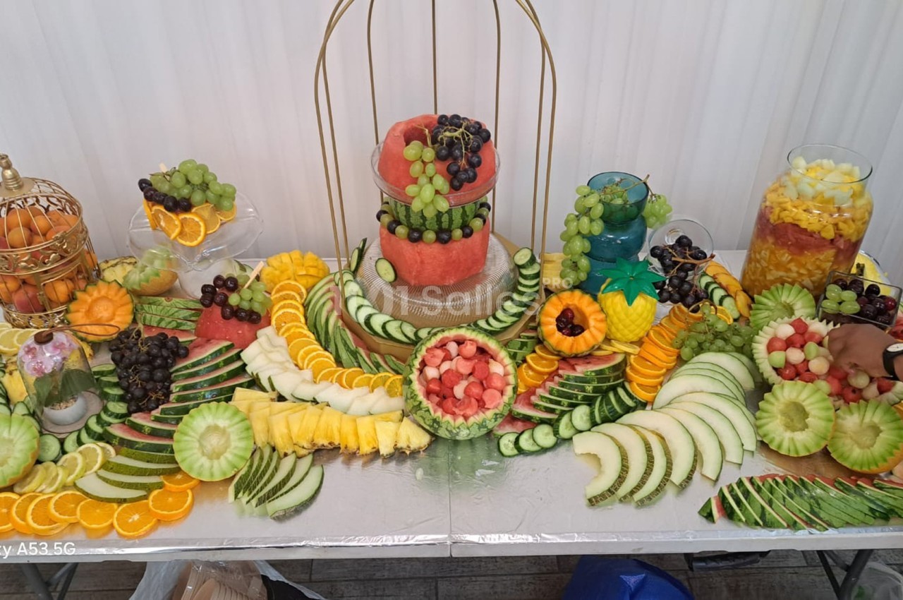 Table garnie de fruits variés découpés et disposés artistiquement, avec pastèques, melons, raisins et agrumes.