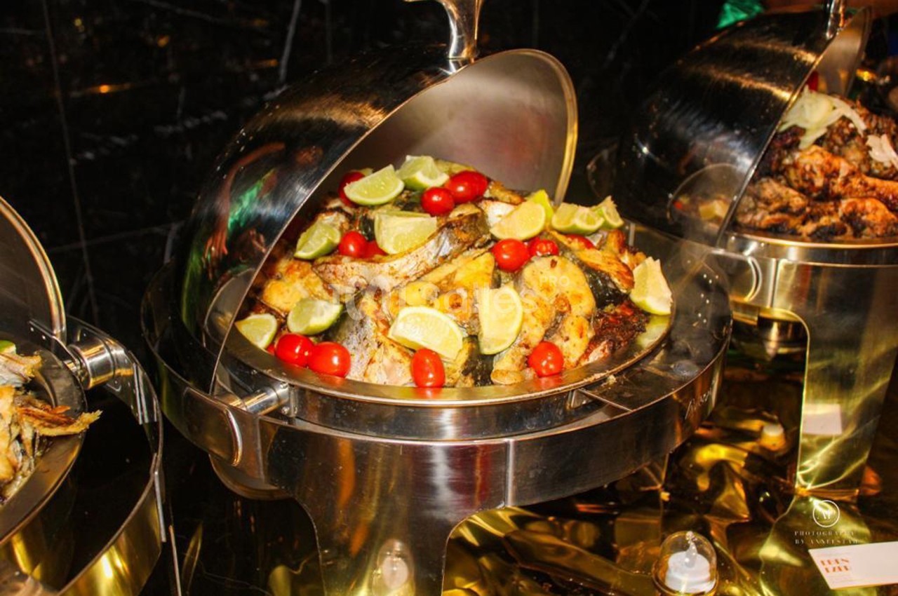 Plat de buffet en inox contenant des morceaux de poisson grillé garnis de quartiers de citron et de tomates cerises.