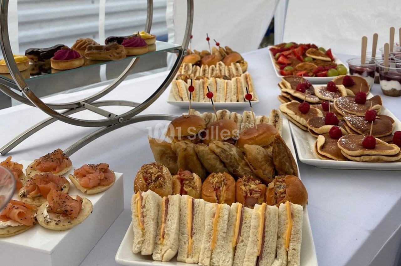 Buffet composé de sandwichs, viennoiseries, fruits, pancakes et verrines, présenté sur une table blanche.