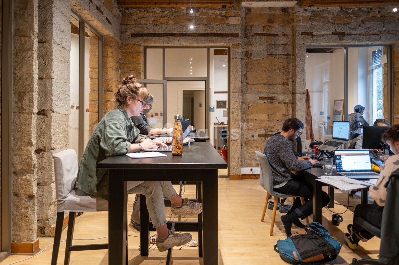 Personnes travaillant sur des ordinateurs dans un espace de coworking avec murs en pierre et mobilier moderne.
