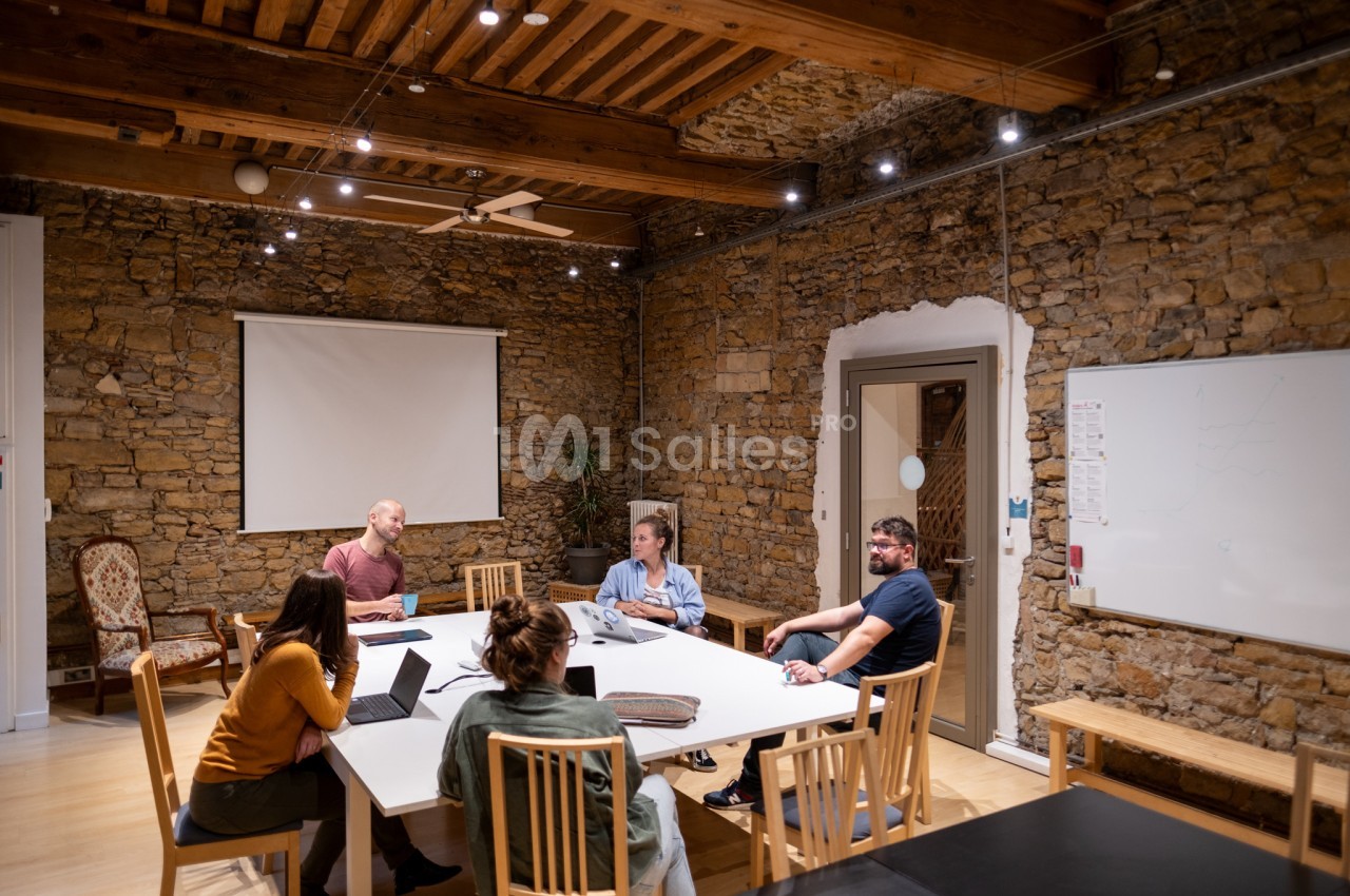 Des personnes discutent autour d'une grande table dans une salle de réunion avec murs en pierre et éclairage chaleureux.