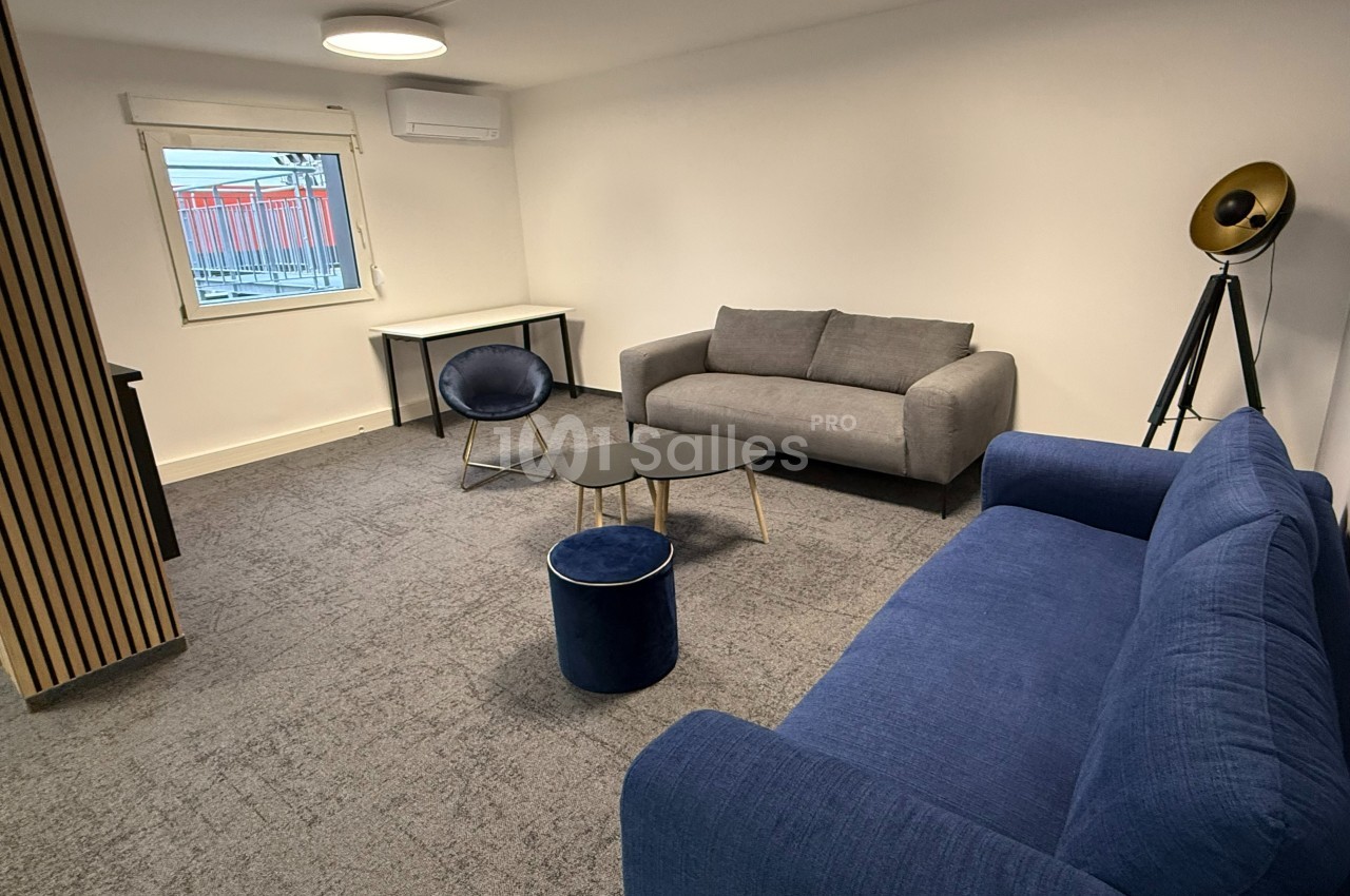Salon moderne avec deux canapés, une table basse, un fauteuil, un tabouret et un lampadaire sur tapis gris.