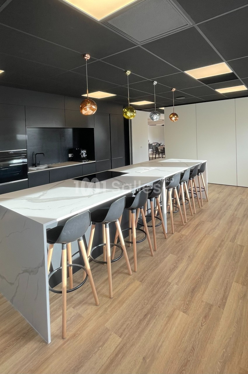 Cuisine moderne avec un long îlot central en marbre, tabourets noirs, éclairage suspendu et sol en bois clair.