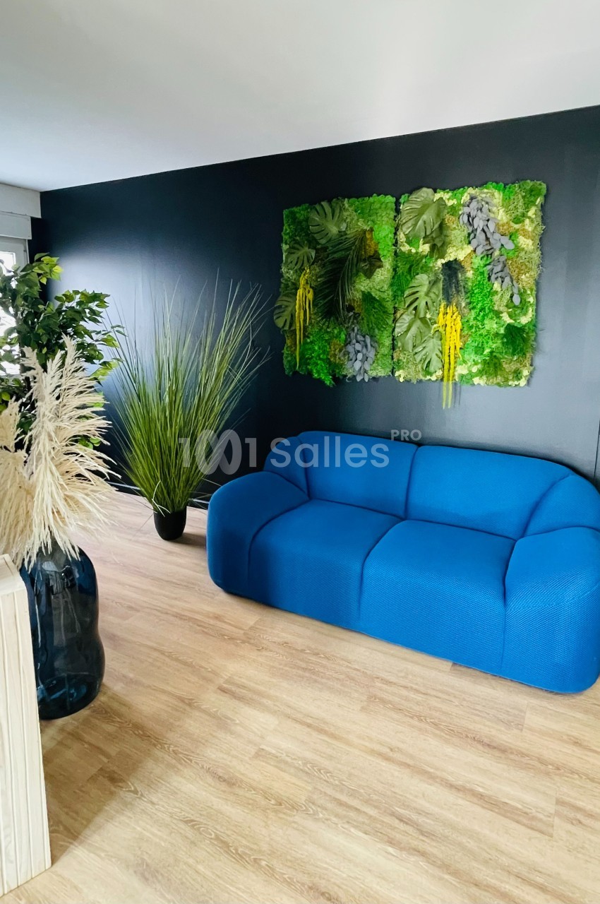Canapé bleu dans un salon moderne avec mur noir, décoration végétale murale et plantes en pots sur sol en bois clair.