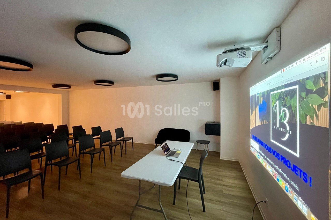 Salle de réunion équipée de chaises, d'une table avec un ordinateur portable et d'un projecteur affichant une présentation.
