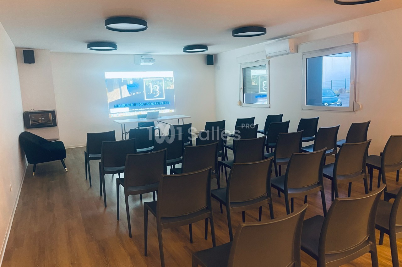 Salle de réunion lumineuse avec rangées de chaises noires, écran de projection allumé et parquet au sol.
