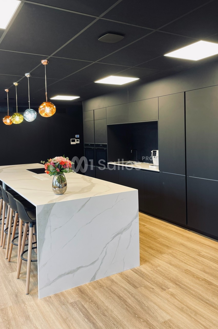 Cuisine moderne avec un îlot central en marbre blanc, chaises hautes, luminaires colorés et armoires noires intégrées.
