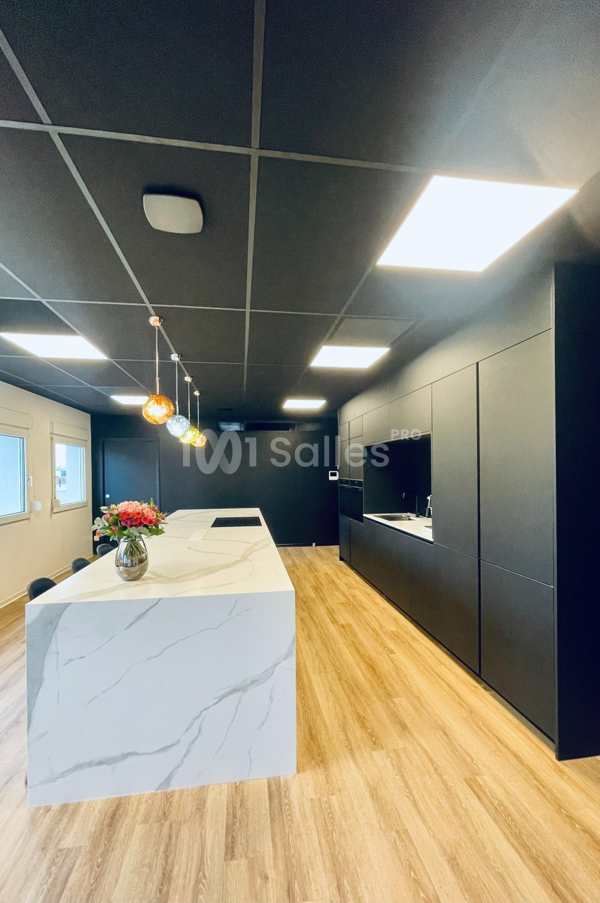 Cuisine moderne avec un îlot central en marbre blanc, éclairage suspendu coloré et mobilier noir mat.