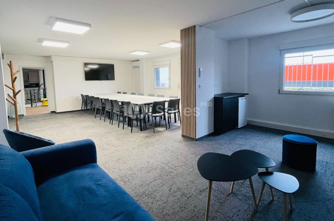 Salle de réunion lumineuse avec une grande table entourée de chaises, un canapé et des tables basses au premier plan.