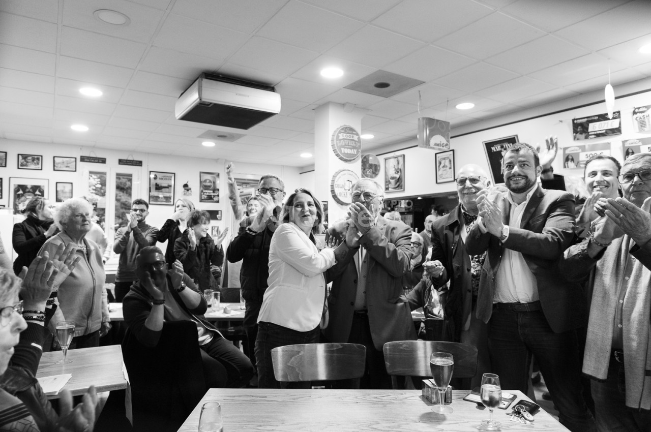 Un groupe de personnes debout dans un café, applaudissant dans une ambiance conviviale.