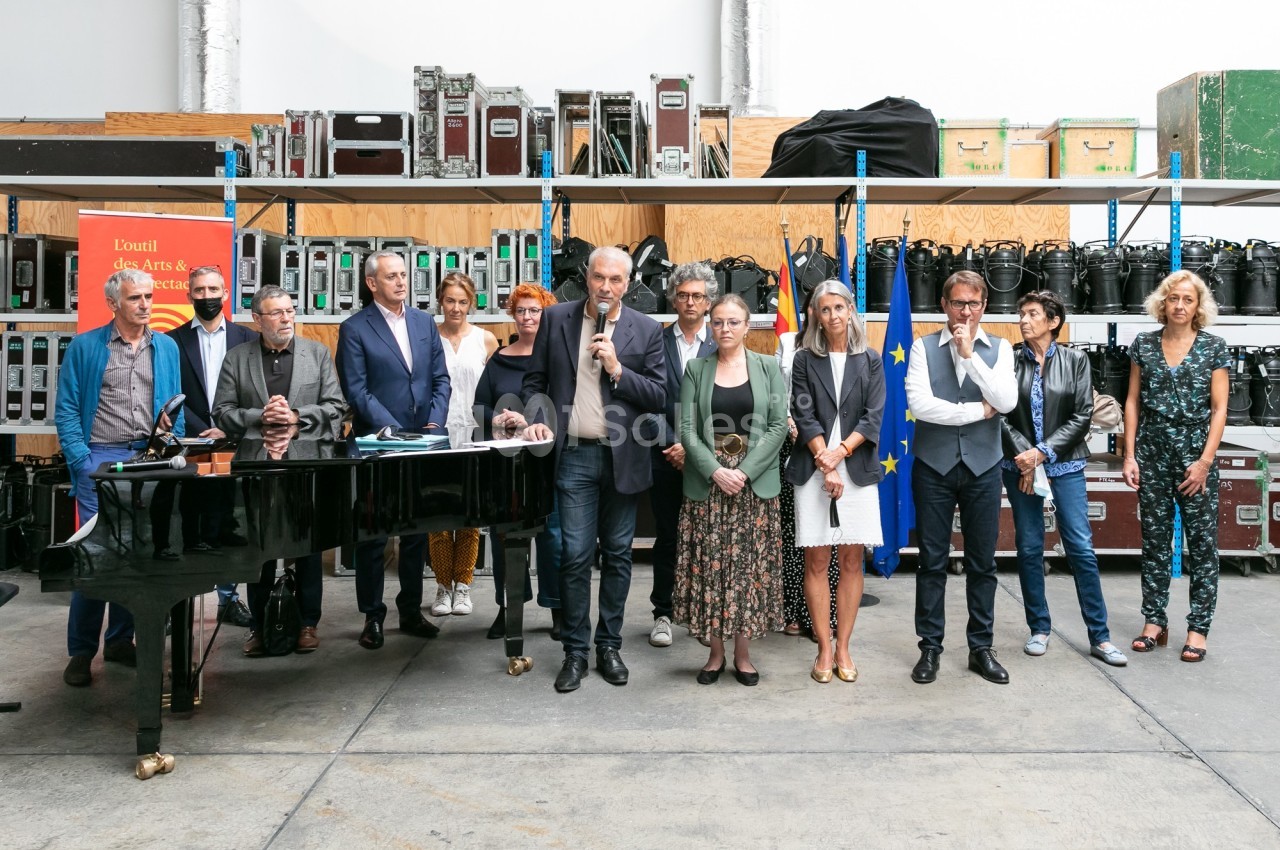 Un groupe de personnes debout dans un espace industriel, avec un piano à queue et des équipements en arrière-plan.