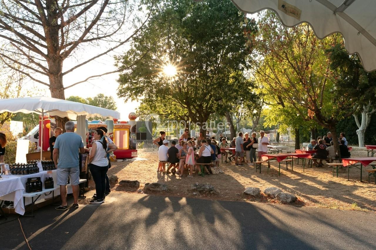Groupe de personnes réunies dans un parc ensoleillé avec stands de nourriture et tables sous les arbres.