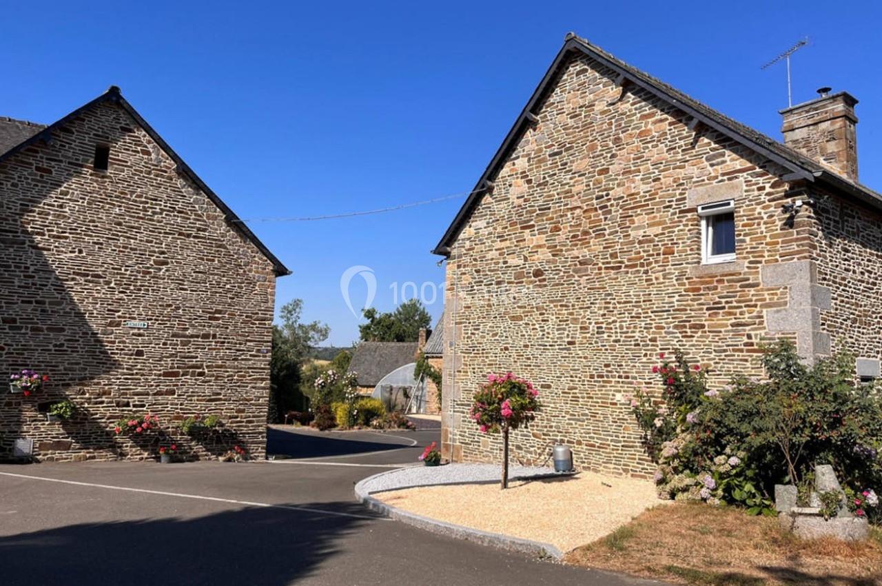 Maisons en pierre dans un village avec ciel bleu, fleurs suspendues et parterre de gravier au premier plan.