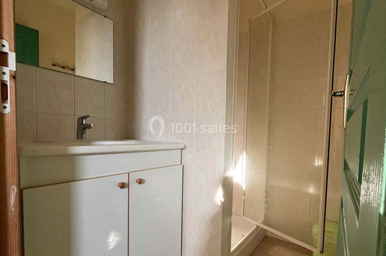 Salle de bain avec lavabo, miroir, meuble blanc et douche à paroi vitrée sur un carrelage beige.