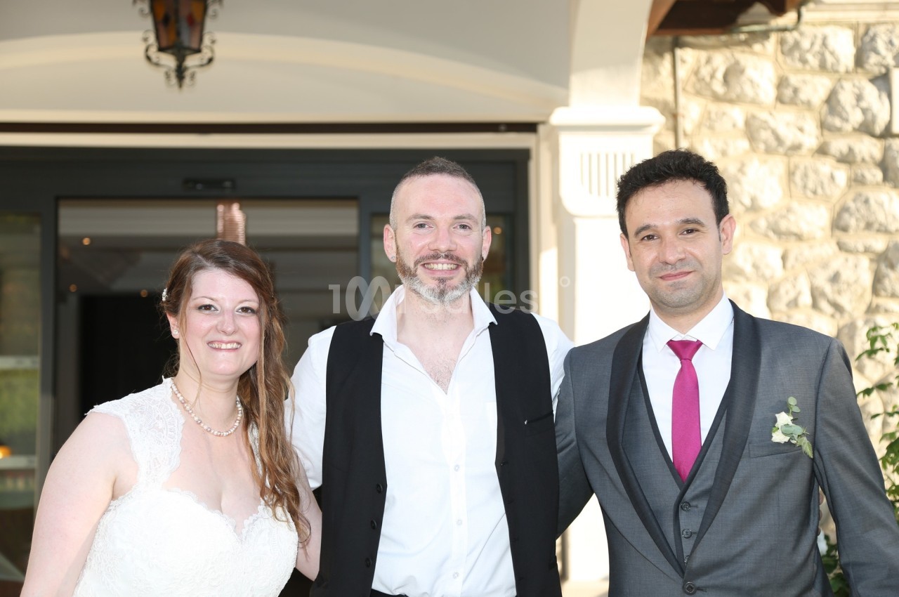 Trois personnes posent ensemble en tenue de mariage devant une entrée de bâtiment en pierre.