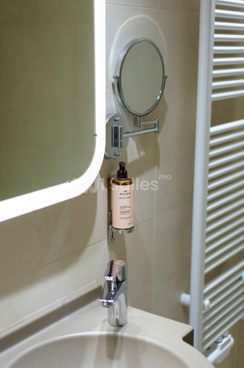 Miroir lumineux, miroir grossissant, distributeur de savon et robinet sur un lavabo dans une salle de bain moderne.