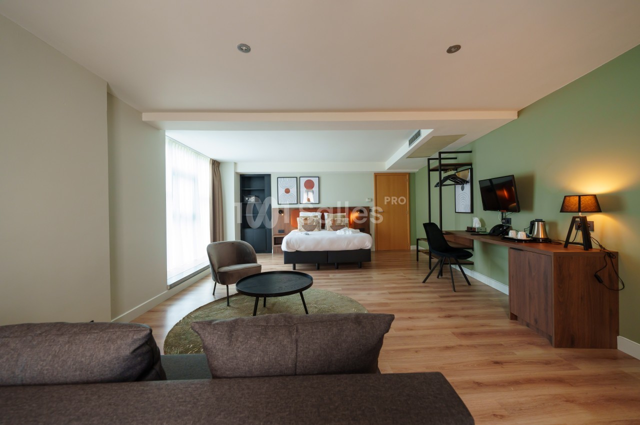 Chambre spacieuse avec lit double, coin salon, bureau, télévision et décoration moderne dans des tons neutres.
