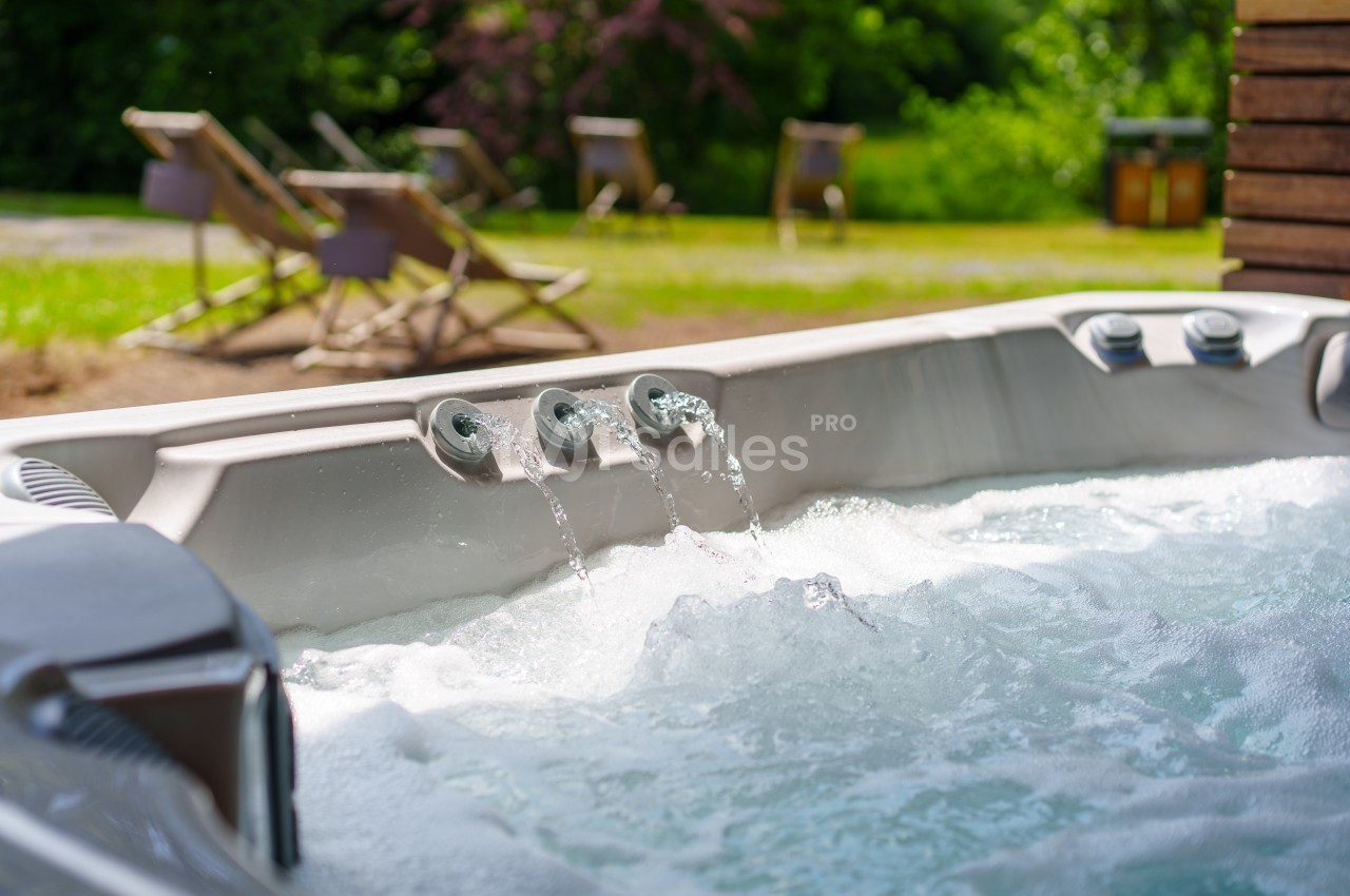 Bain à remous extérieur avec jets d'eau, entouré de chaises longues et d'un jardin verdoyant en arrière-plan.