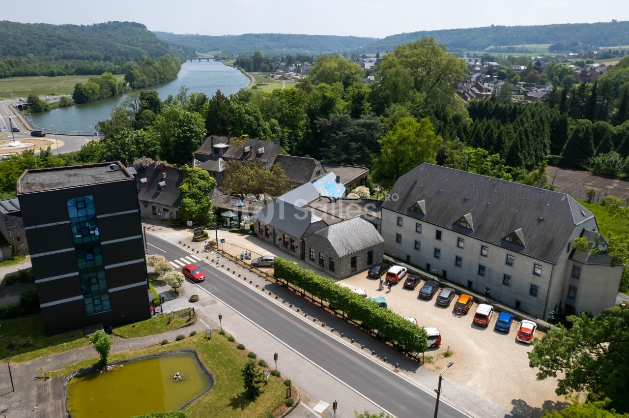 Vue aérienne d'un complexe de bâtiments entouré de verdure, avec une route et une rivière à proximité.