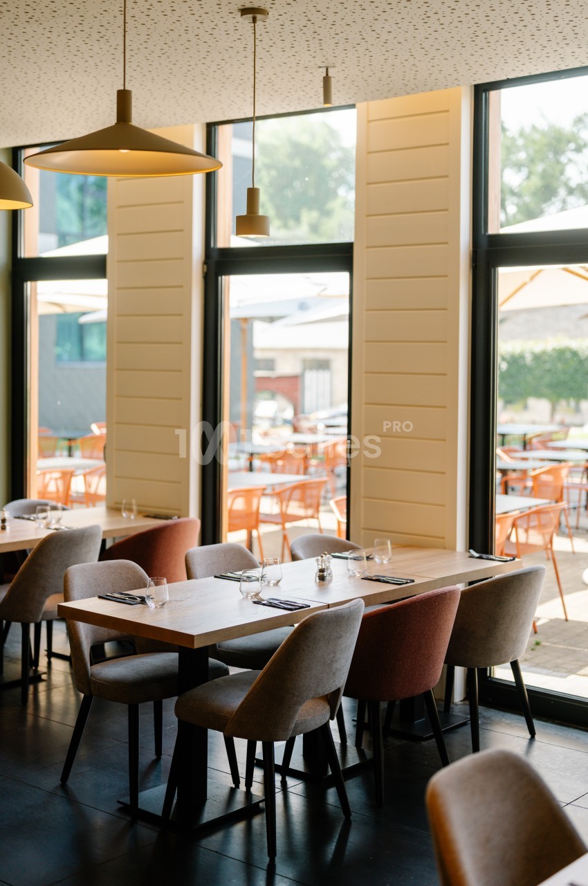 Salle de restaurant lumineuse avec des tables dressées, des chaises colorées et vue sur une terrasse extérieure.
