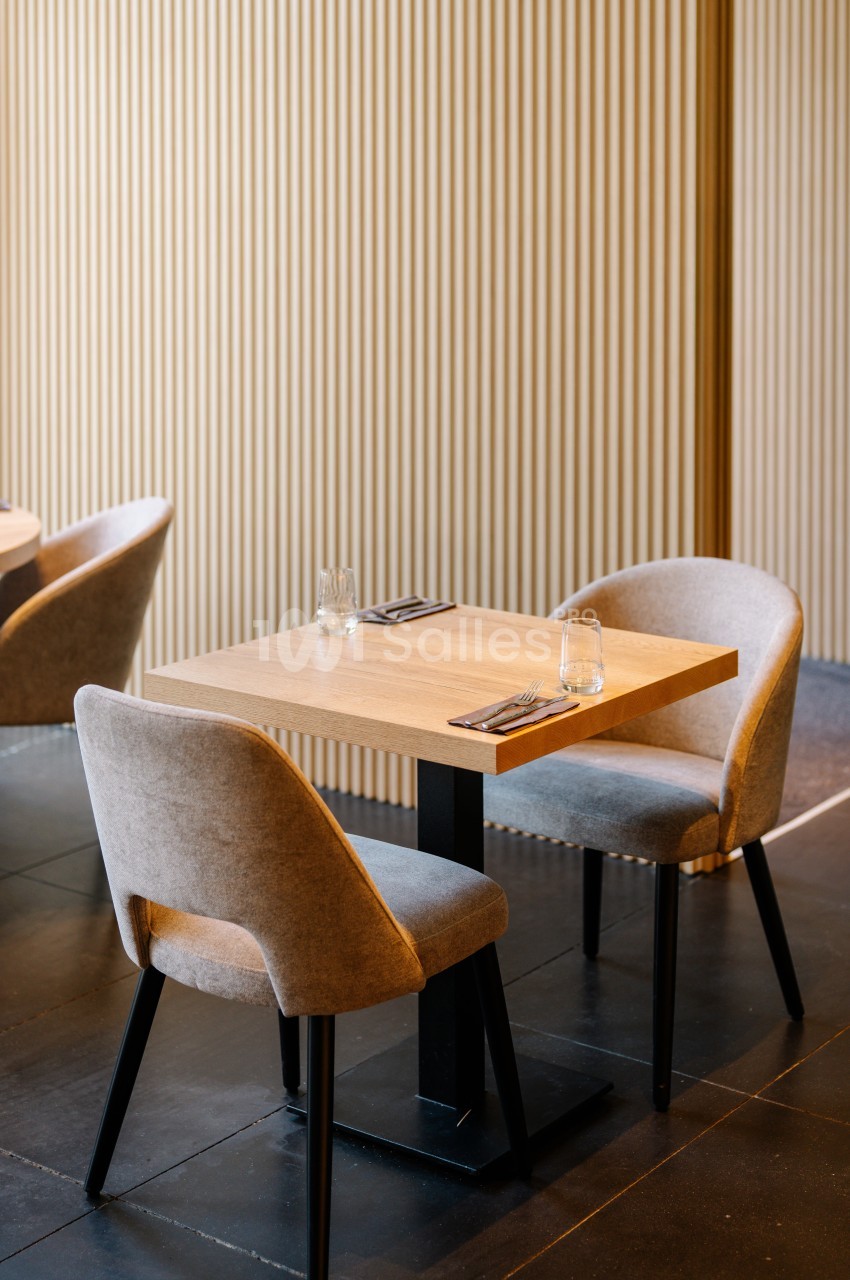 Table en bois pour deux personnes avec chaises rembourrées, dressée avec couverts et verres, dans un intérieur moderne.