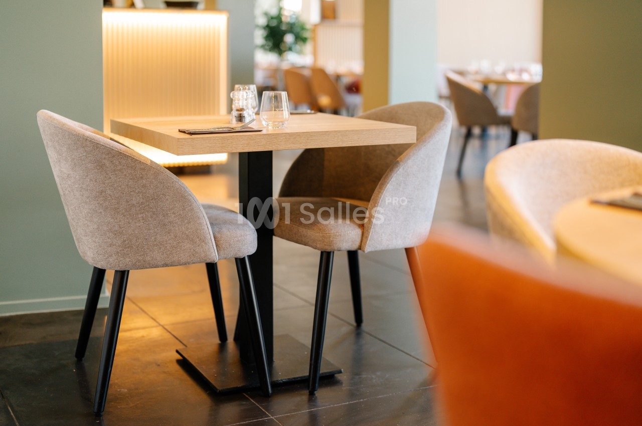 Table en bois avec deux chaises rembourrées dans un restaurant lumineux au sol en carrelage foncé.