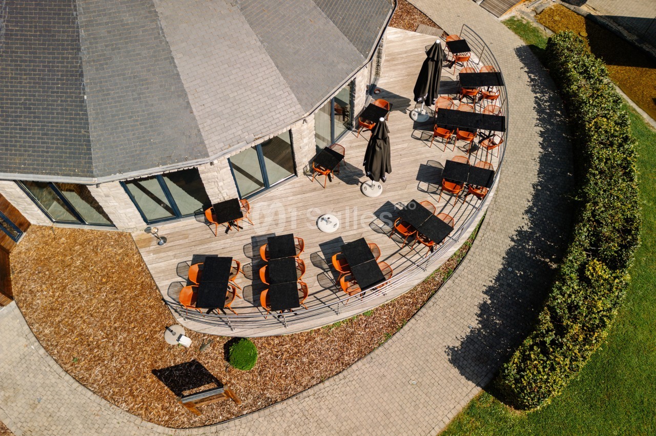 Terrasse extérieure avec tables et chaises disposées autour d’un bâtiment circulaire, vue aérienne.
