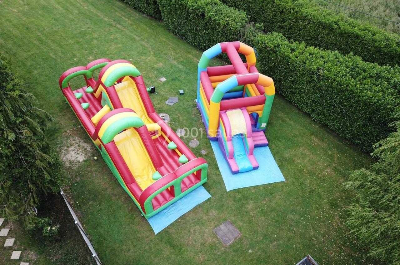 Deux structures gonflables colorées installées sur une pelouse, entourées de haies et d'arbres.