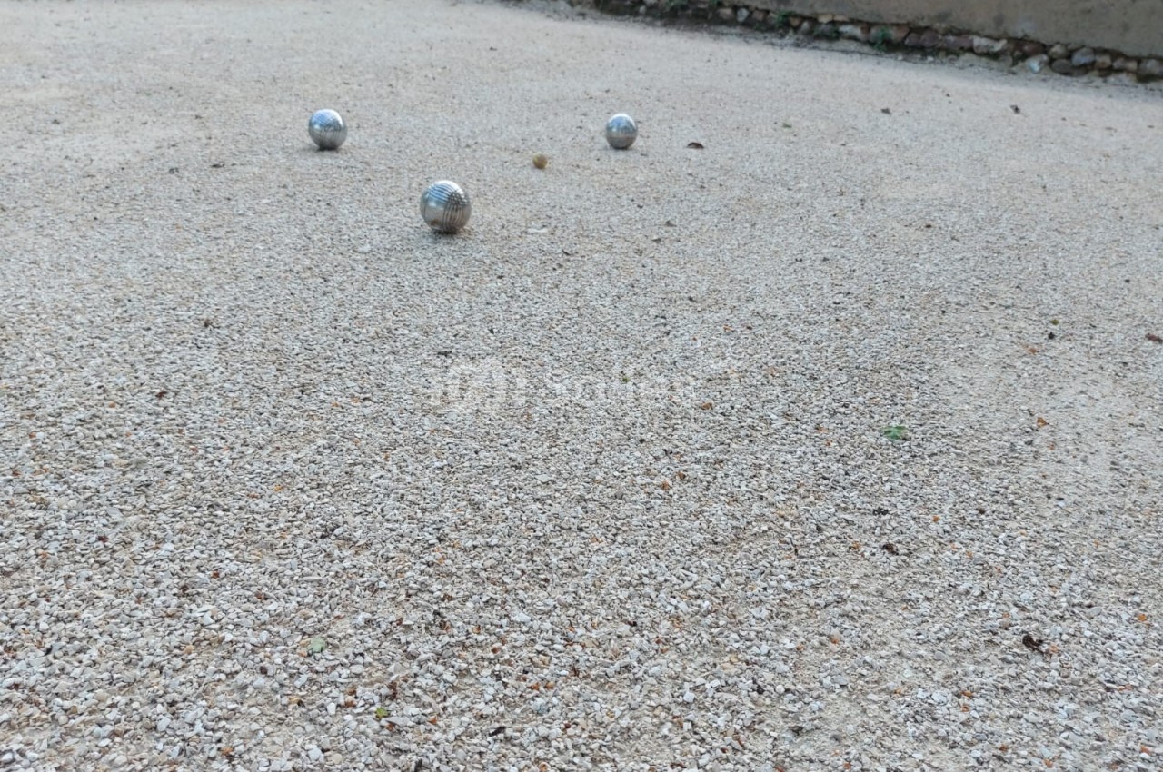 Trois boules de pétanque posées sur un terrain en gravier.