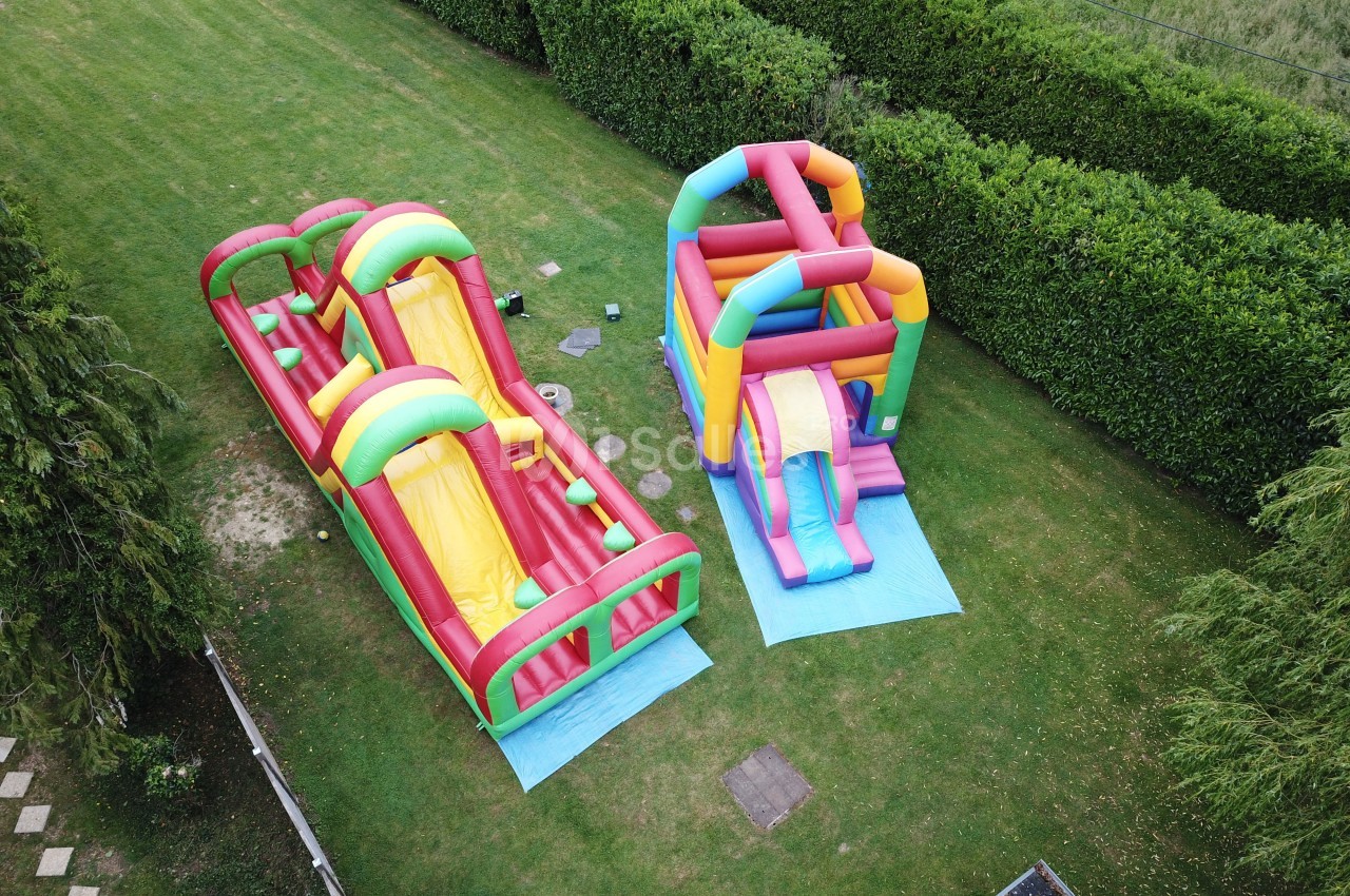 Deux structures gonflables colorées installées sur une pelouse, entourées de haies et d'arbres.